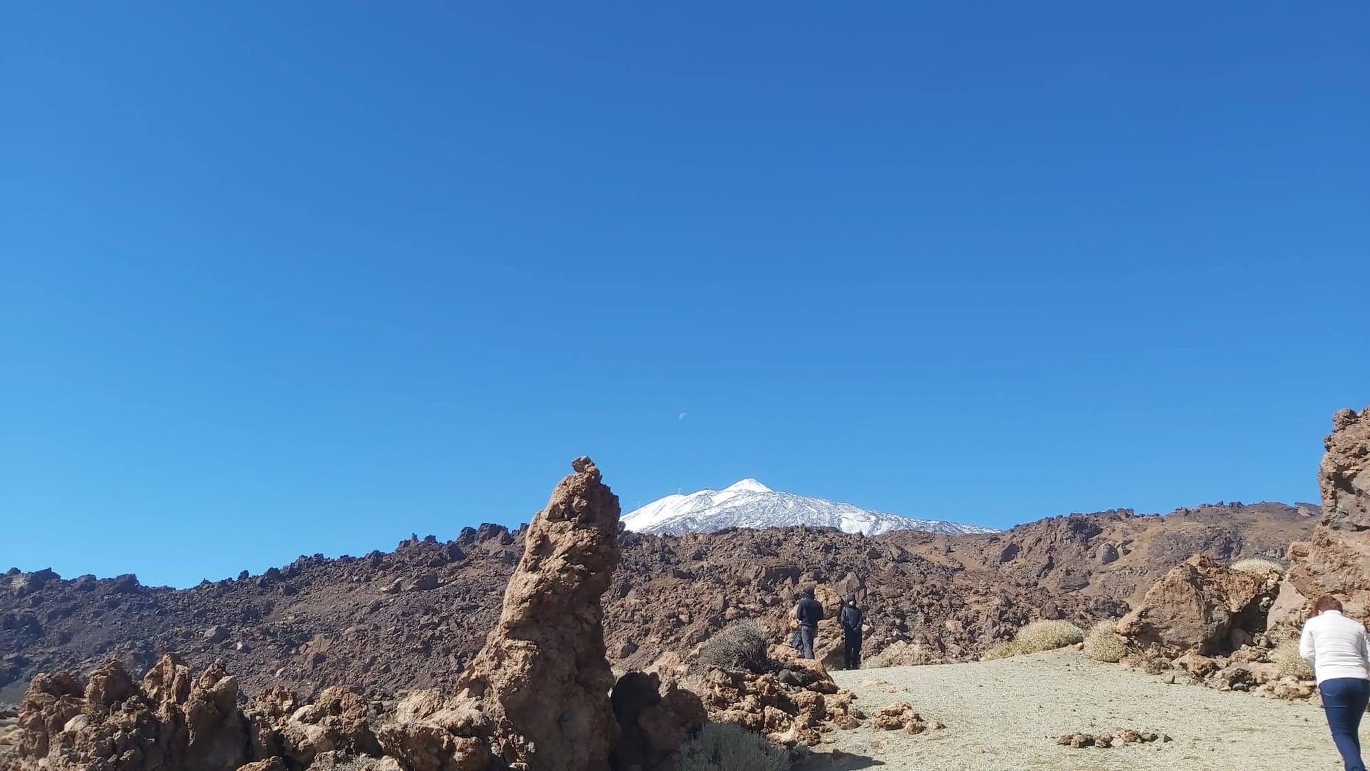 Paisaje volcánico con formaciones rocosas y el pico del Teide nevado al fondo.